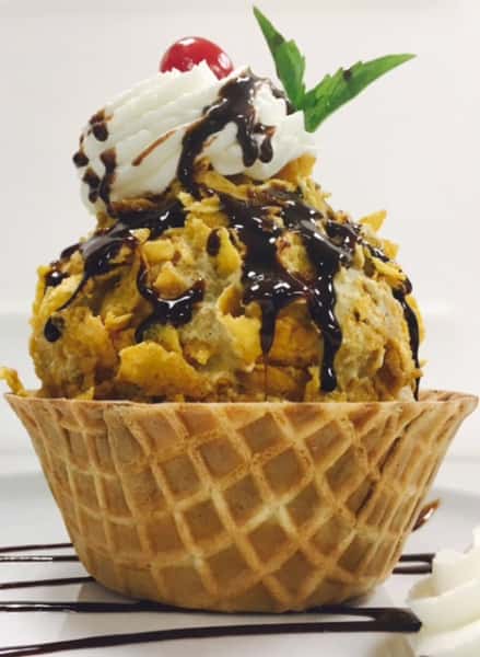 Ice cream in waffle bowl topped with whipped cream and chocolate syrup
