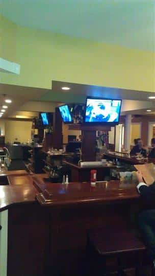 angle of bar with three tv's and customers sitting around the bar