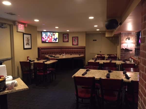 tables and chairs in dining room with a booth in the back below a tv on the wall