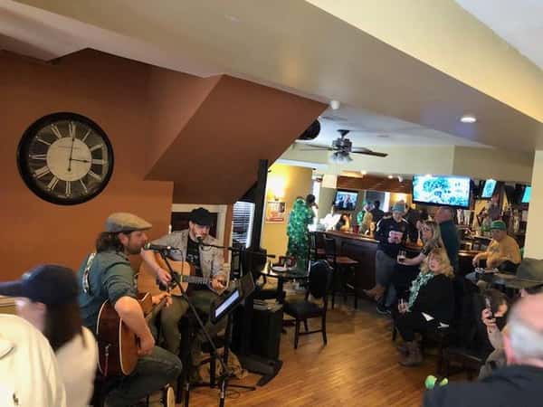 two men playing guitars in front of people sitting at the bar