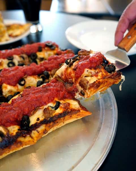 Thick crust square pizza on a tray. Spatula scooping an end piece up for serving