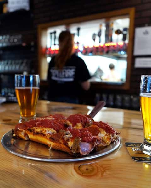 pepperoni pizza and a glass of beer sitting on the top of the bar.