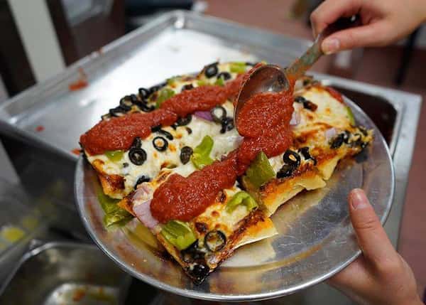 Personal size thick pizza topped with bell peppers, olives and marinara sauce on a tray
