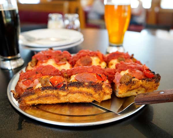 thick crust pizza with pepperoni on a pan in front of a mug of beer