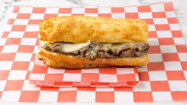 Hot roast beef sandwich with melted provolone cheese served on a toasted hoagie roll, placed on red and white checkered deli paper.