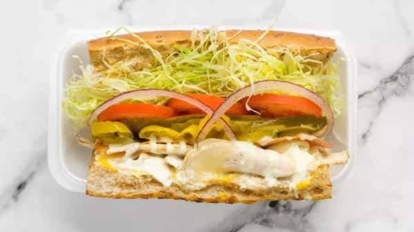 Fresh deli sub sandwich loaded with shredded lettuce, sliced tomatoes, pickles, banana peppers, red onion, and melted cheese over turkey, served on a toasted hoagie roll in a takeout container.