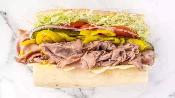 Fresh roast beef sub sandwich loaded with shredded lettuce, tomato slices, pickles, banana peppers, and melted cheese on a soft hoagie roll.