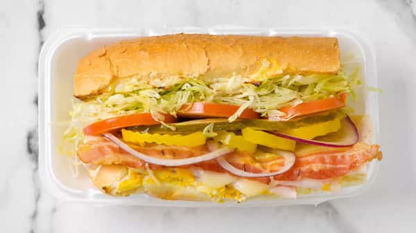 Crispy bacon and cheese sub sandwich with shredded lettuce, tomato slices, banana peppers, pickles, and red onion on a toasted hoagie roll.