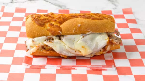 Hot Italian beef sandwich with melted provolone cheese and savory beef slices on a toasted cheese-crusted hoagie roll, served on red checkered deli paper.