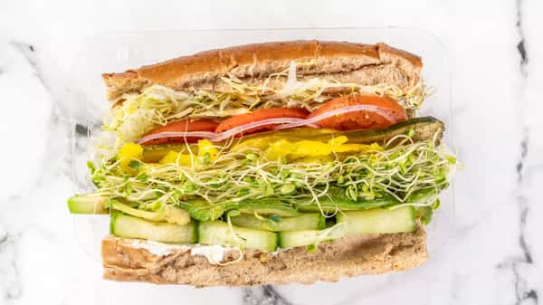 Fresh veggie sub sandwich with cucumber slices, avocado, sprouts, shredded lettuce, tomato, banana peppers, pickles, and red onion on whole wheat bread.