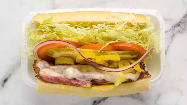 Toasted deli sub sandwich layered with melted cheese, thinly sliced cured meats, shredded lettuce, tomato slices, banana peppers, and red onion on a hoagie roll.