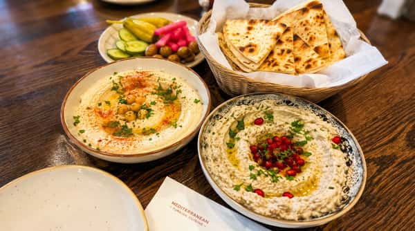 Creamy hummus and smoky babaganoush mezze served with warm pita bread, olives, and Mediterranean pickles
