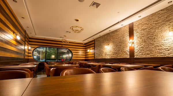Restaurant interior with brown leather chairs, dark wood tables, striped wood walls, and a stone accent wall.