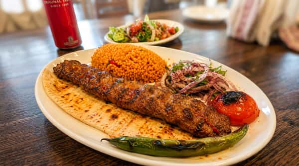 Grilled lamb Adana kebab served with bulgur rice, grilled tomato, onions, and charred peppers on warm flatbread