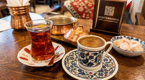 Traditional Turkish tea and rich Turkish coffee served with Turkish delight on ornate ceramic cups and copper tableware in a cozy Mediterranean restaurant