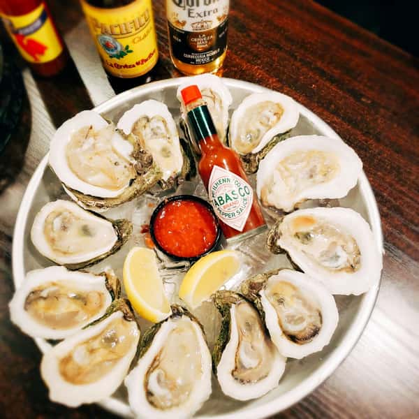 Oysters in a bowl over ice with hot sauce in the center