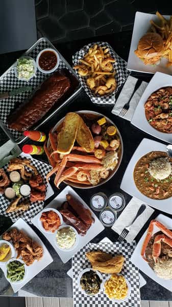 A table filled with multiple dishes such as ribs, a seafood bowl, wings and gumbo