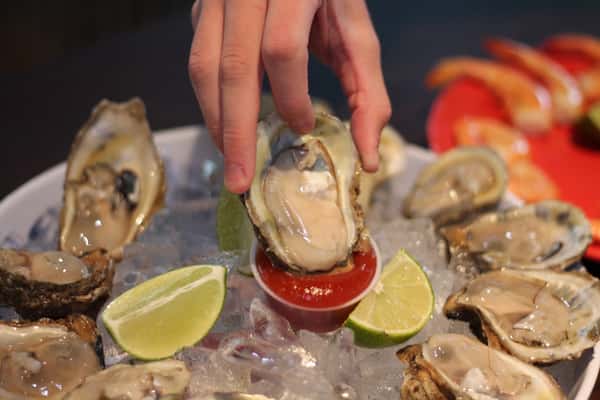 A hand dipping an oyster into sauce