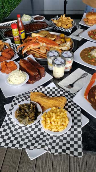 A table filled with multiple dishes such as ribs, a seafood bowl, wings, macaroni and cheese, fried chicken and green beans