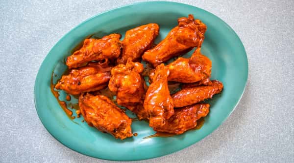 Spicy buffalo chicken wings on a teal oval plate, with orange sauce pooling on the plate.