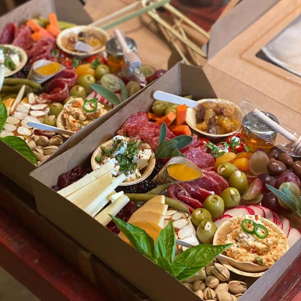 two charcuterie boards with assorted meats, cheeses, fruits, vegetables, crackers and nuts in boxes