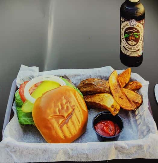 Burger with lettuce, tomato, pickles and onions served with thick-cut fries, ketchup, and a chocolate stout beer.