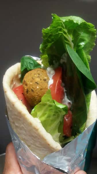Falafel wrap filled with fresh lettuce, tomato, spinach, and tahini sauce in a pita.
