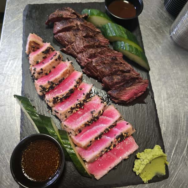 Seared ahi tuna and grilled steak slices served with cucumber, wasabi, and dipping sauces on a black slate plate