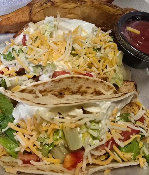 Chicken tacos with lettuce, shredded cheese and sour cream, served with potato wedges and ketchup.