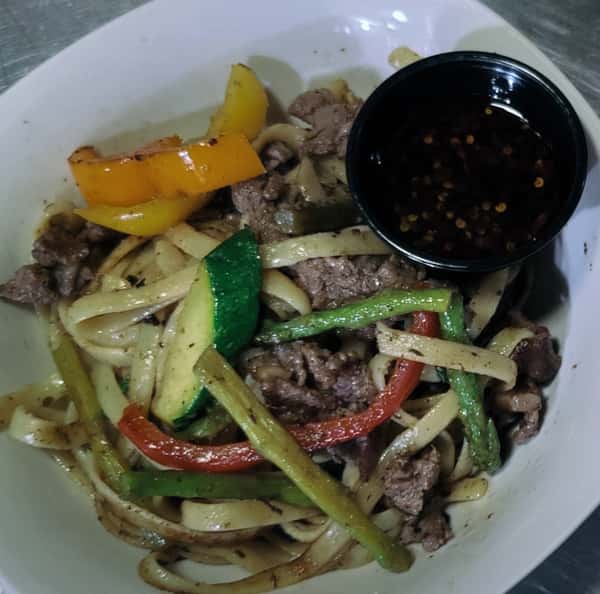 Beef stir-fry with noodles and sautéed vegetables in a white bowl