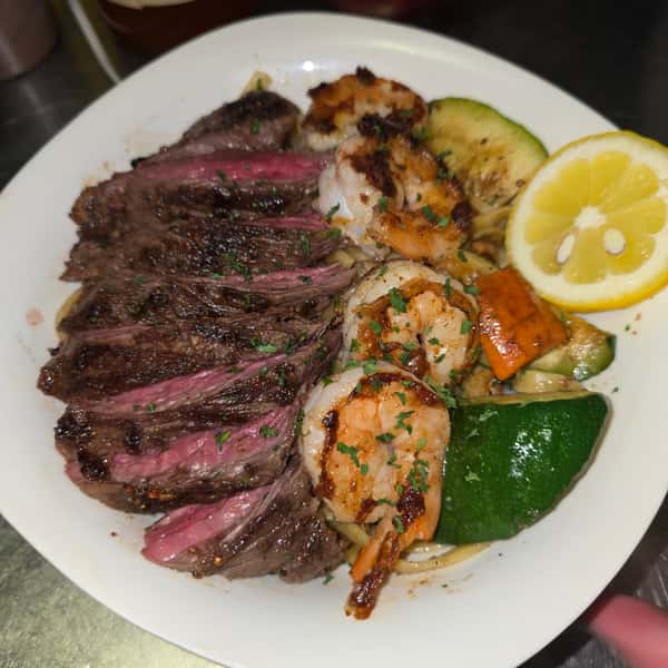 Grilled steak and shrimp with sautéed vegetables and lemon on a white plate