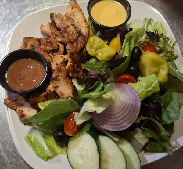 Grilled chicken breast with fresh garden salad and assorted dressings on the side.