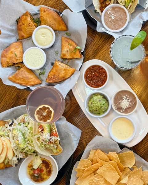 A vibrant table with tacos, appetizers, and drinks, set in a lively restaurant atmosphere.