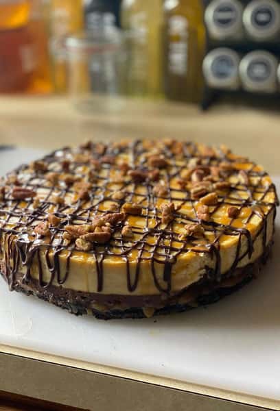 Caramel pecan cheesecake with a chocolate cookie crust, drizzled with chocolate and topped with whole pecans.