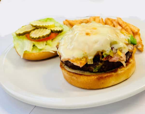 Cheeseburger topped with grilled vegetables and melted cheese, served with lettuce, tomato, pickles, and a side of fries.