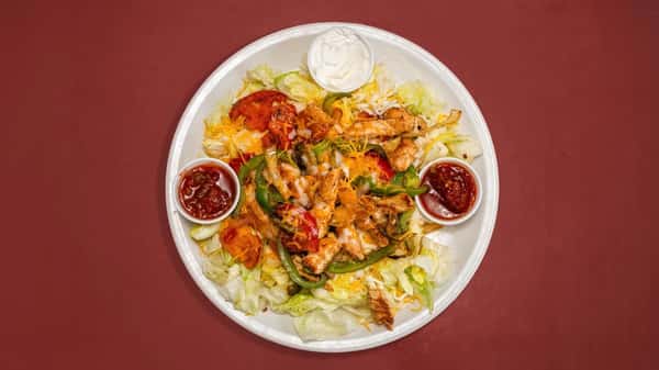This dish is a hearty fajita-style chicken salad, featuring grilled chicken strips, sautéed green peppers, onions, and tomatoes atop a bed of shredded iceberg lettuce and melted cheese. It's served with a dollop of sour cream and two portions of chunky salsa on the side for added flavor.