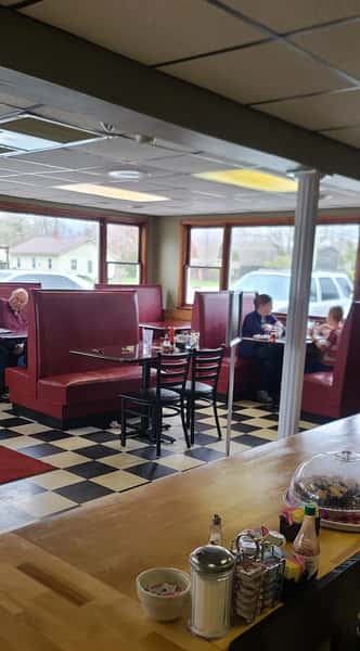 Diner interior with red booths, checkered floors, and large windows; guests are seated and eating near the wooden counter.