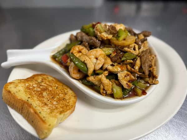 Stir-fry with shrimp, chicken, beef, and bell peppers in savory sauce, served with a slice of toasted garlic bread.