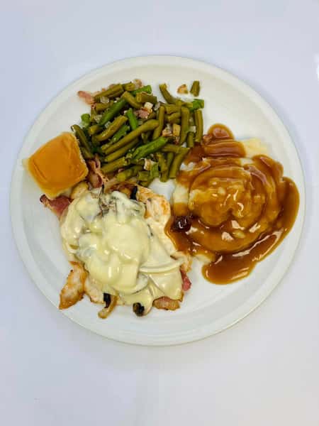 Grilled chicken breast with melted cheese and mushrooms, mashed potatoes with brown gravy, green beans, and a dinner roll.