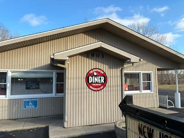 Tan building exterior with "The Huntington Diner" sign, labeled 1901, under a clear blue sky with trees in the background.