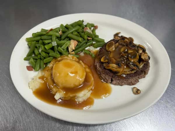 Salisbury steak topped with mushroom gravy, served with mashed potatoes and green beans with bacon.