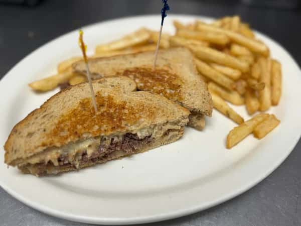Grilled Reuben sandwich on rye bread with melted cheese and corned beef, served with golden French fries.