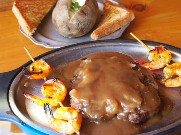 steak with gravy and shrimp skewers with a baked potato on the side