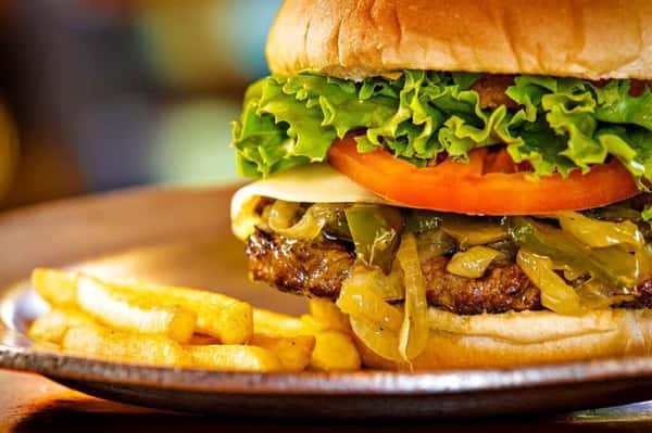 burger on a bun with ham, pineapple slices, tomatoes and lettuce with a side of fries