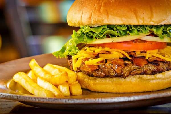 burger on a bun with ham, pineapple slices, tomatoes and lettuce with a side of fries