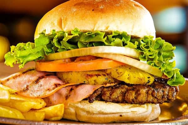 burger on a bun with ham, pineapple slices, tomatoes and lettuce with a side of fries