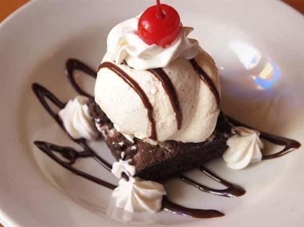brownie topped with ice cream, syrup, whipped cream and a cherry