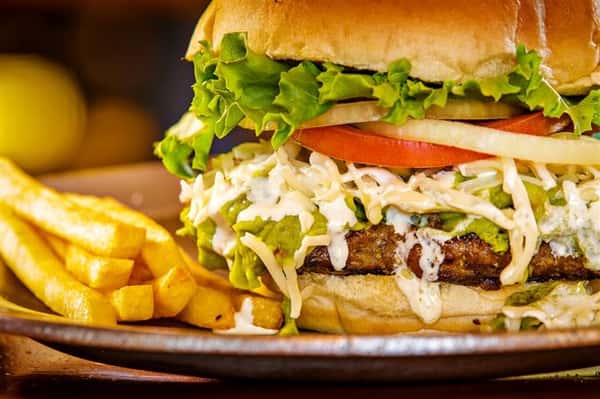 burger on a bun with ham, pineapple slices, tomatoes and lettuce with a side of fries
