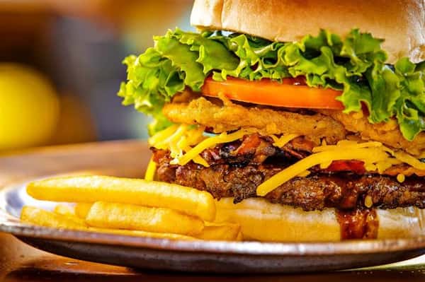 burger on a bun with ham, pineapple slices, tomatoes and lettuce with a side of fries