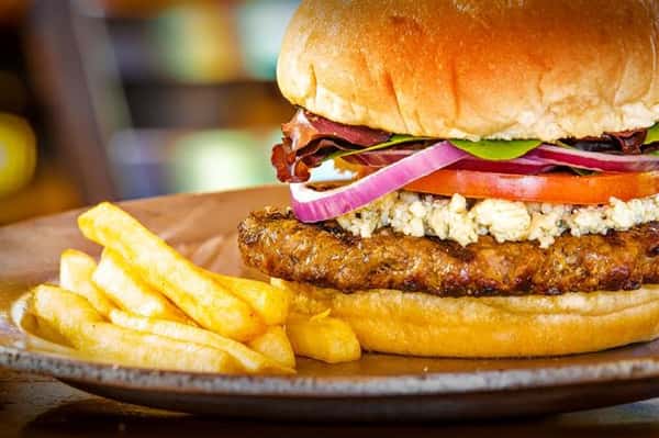 burger on a bun with ham, pineapple slices, tomatoes and lettuce with a side of fries